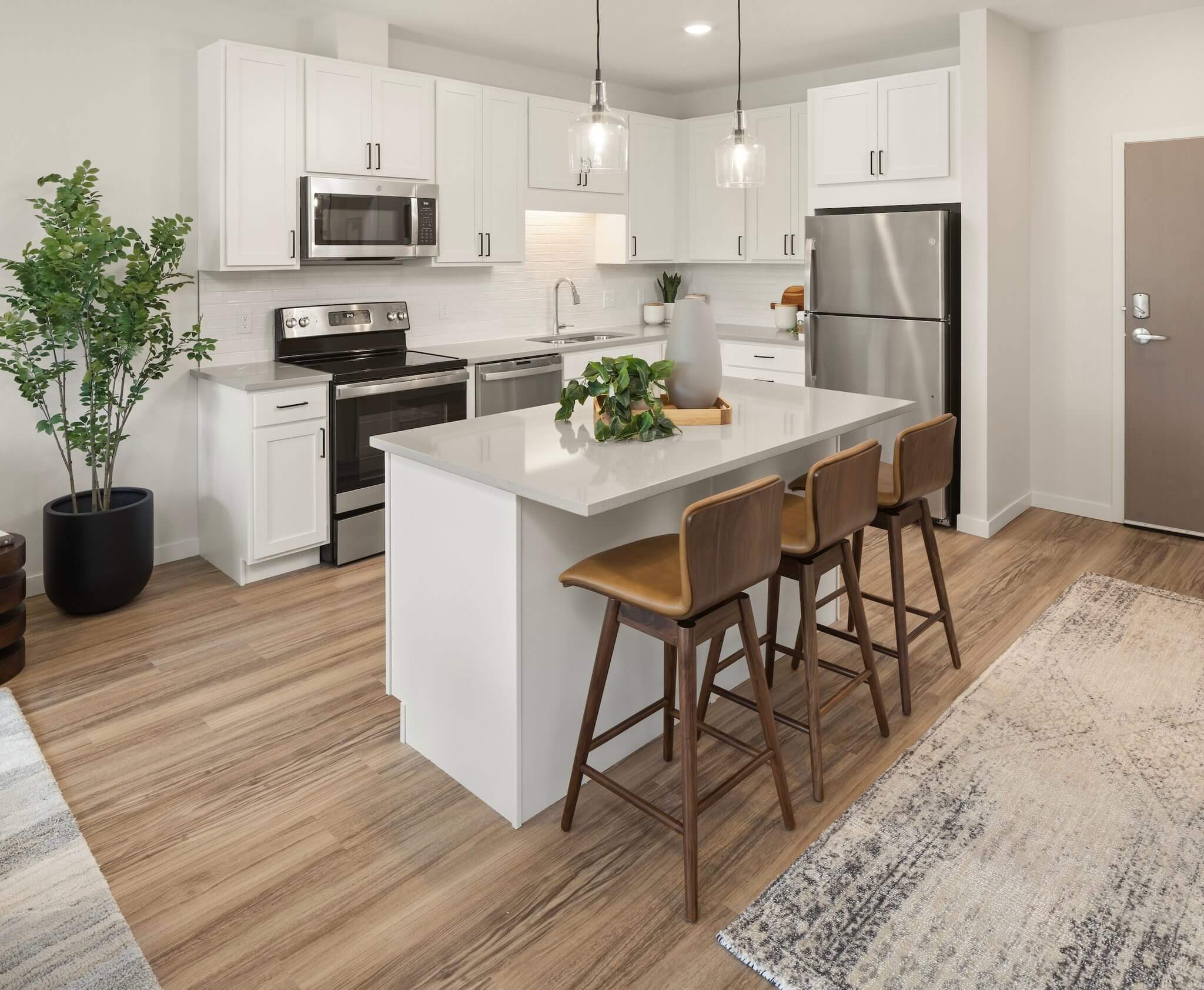 Aster at Riverdale Station apartment kitchen with kitchen island, barstools, pendant lighting, and stainless steel appliances