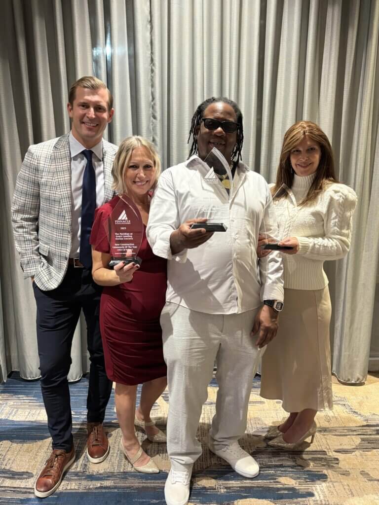 Four people in formal attire smile, holding awards, standing in front of a curtain.
